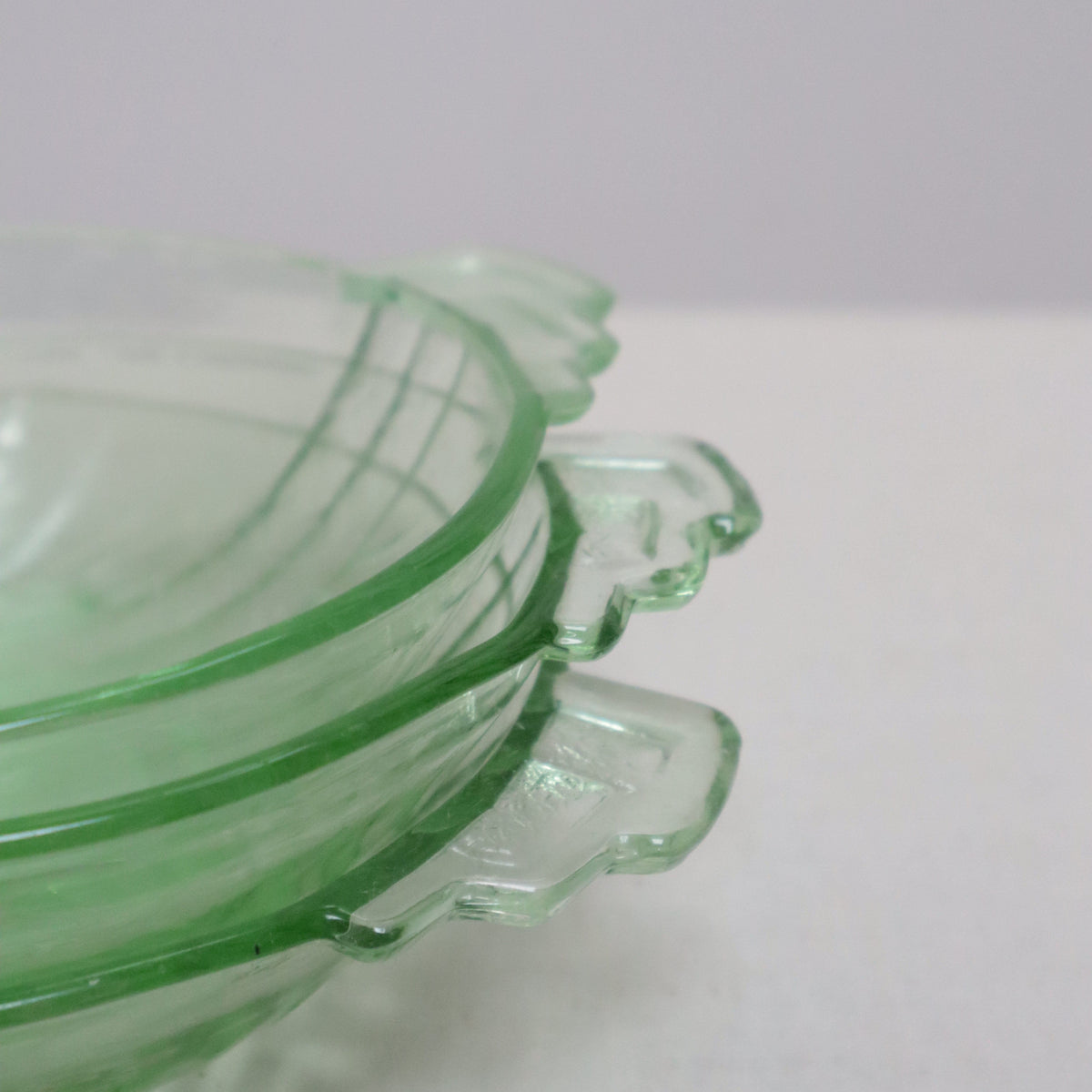 A close-up of a translucent light green glass object with a scalloped top edge, photographed against a plain off-white wall.
