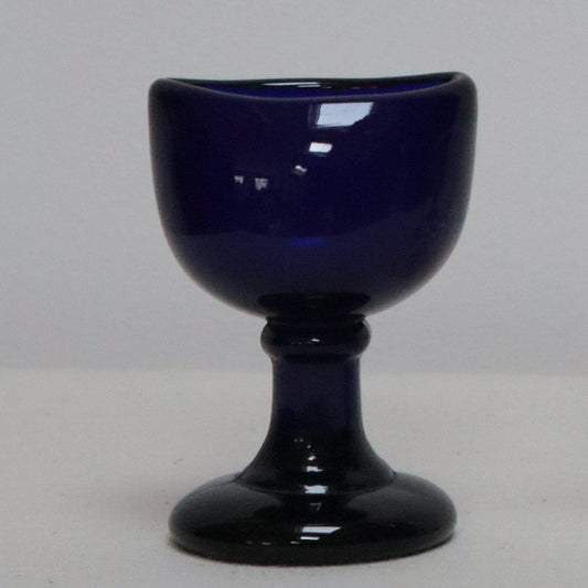 A small blue glass bud vase or goblet cup made of coloured glass, shown side by side on a light grey surface against a light grey background. 