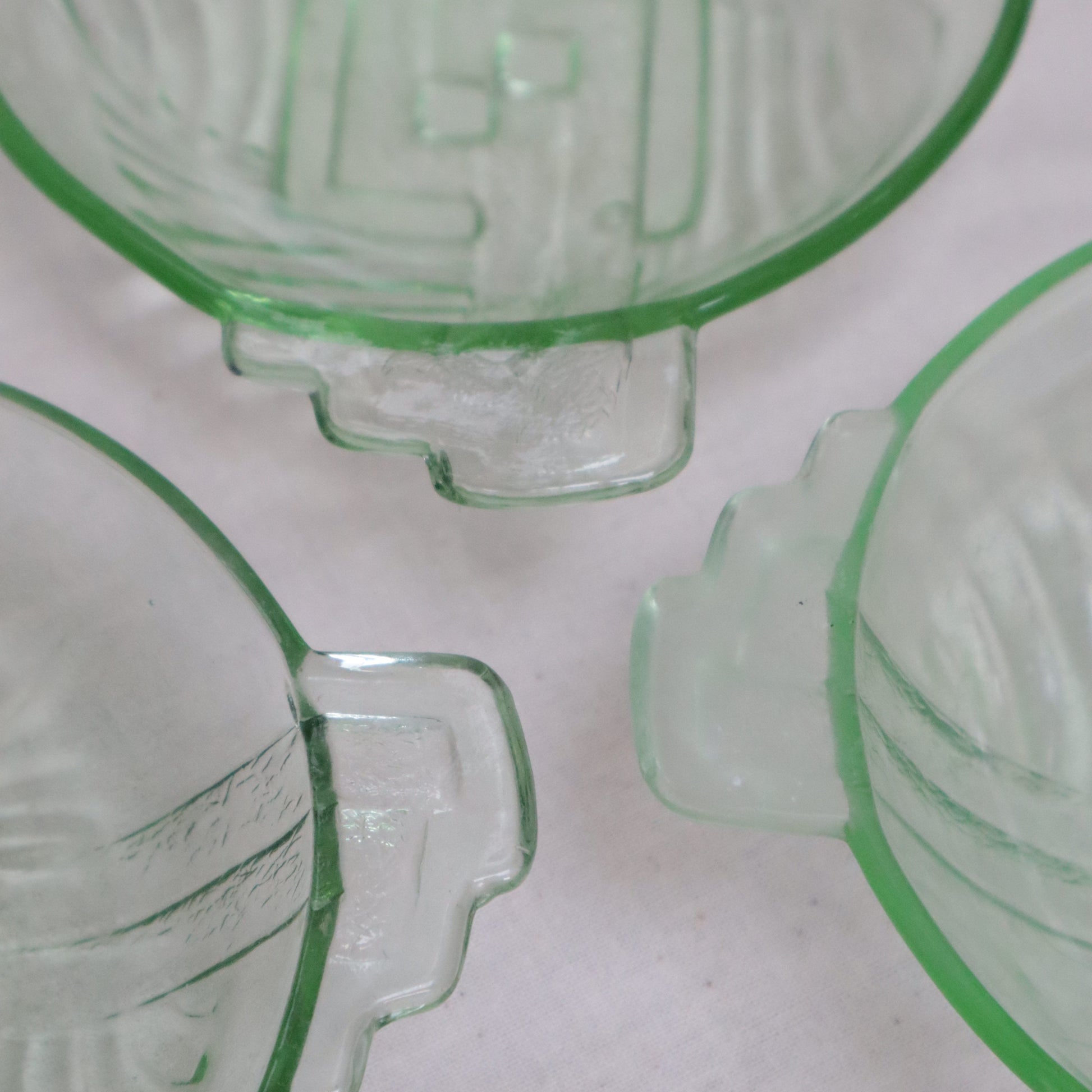 Three vintage green-tinted clear glass bowls with embossed geometric patterns and integrated handles, arranged on a light textured background.