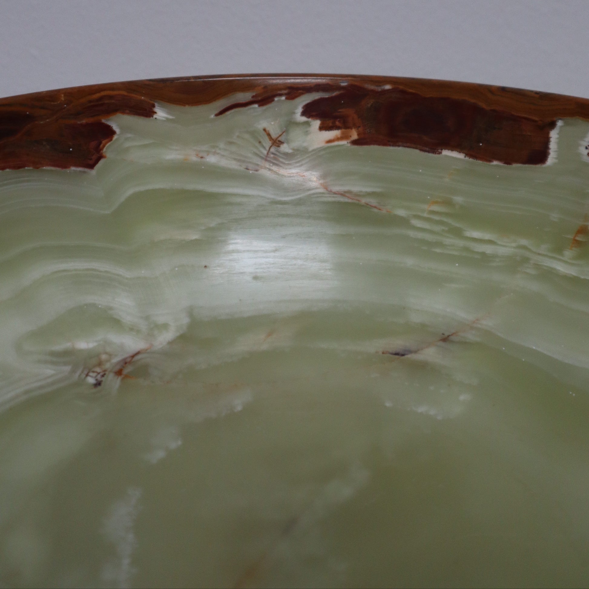A close-up of a polished stone onyx bowl with a creamy green centre and a natural brown edge, shown against a plain light grey background.