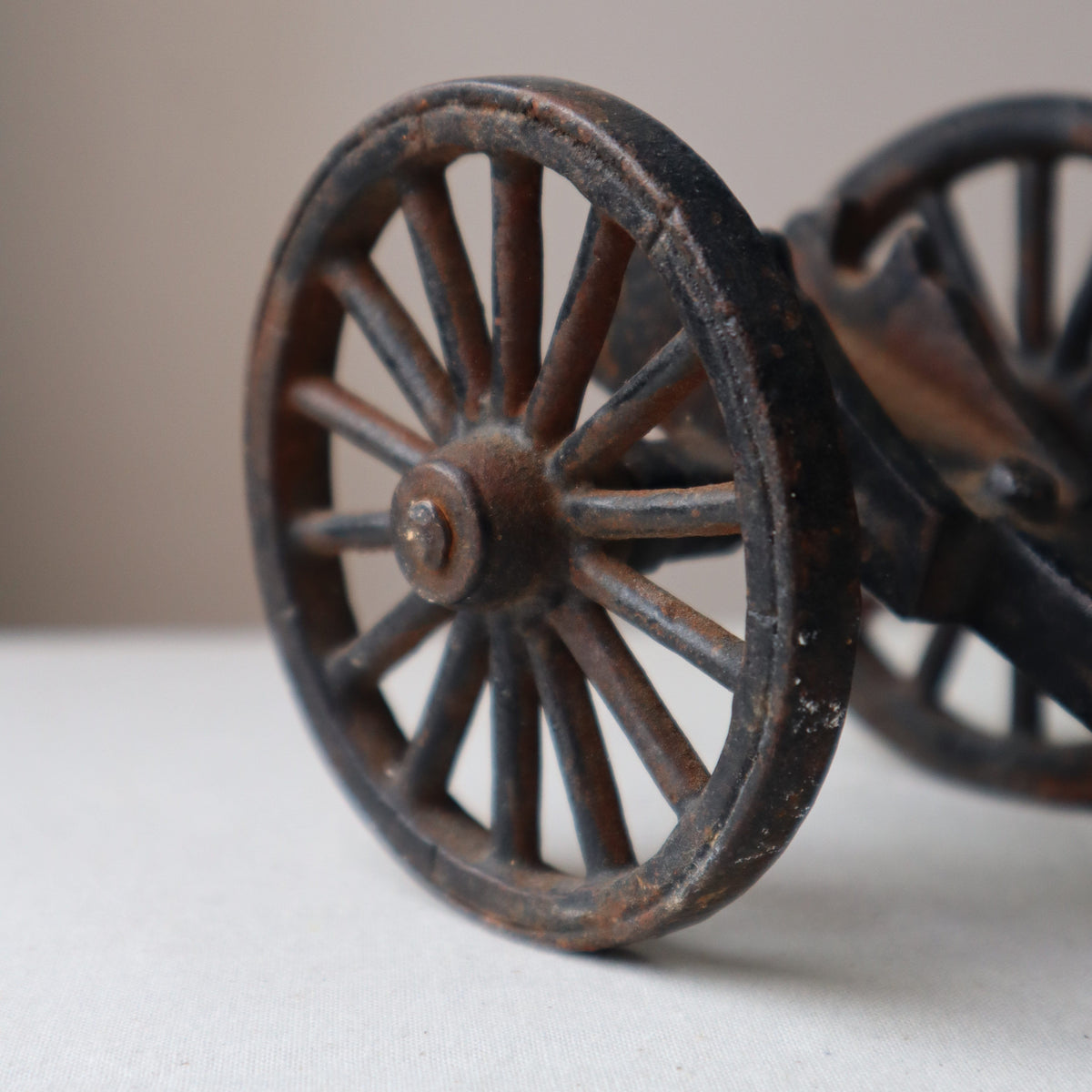 A close-up of a dark, vintage-style metal wagon wheel ornament or wall decor against a plain off-white wall.