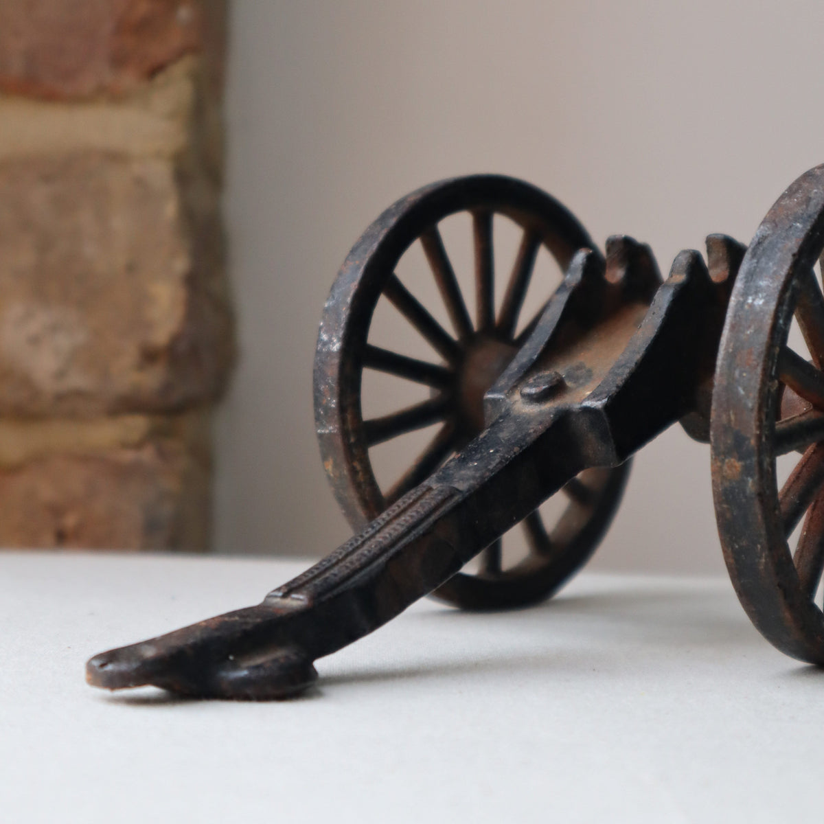 A close-up of a dark metal decorative wall mount shaped like vintage wagon wheels, attached to a white wall above a rustic stone surface.