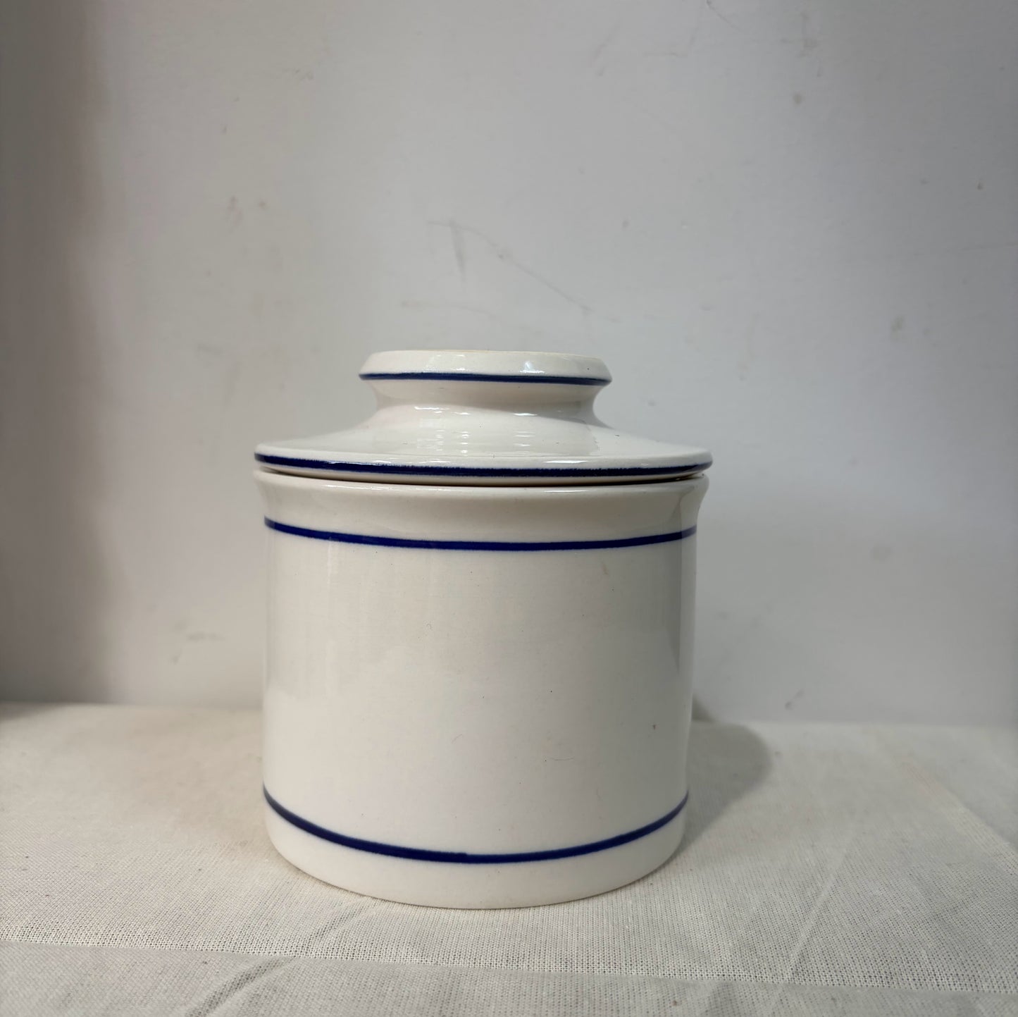 A white ceramic French butterbell or butter crock decorated with two thin blue horizontal stripes. 