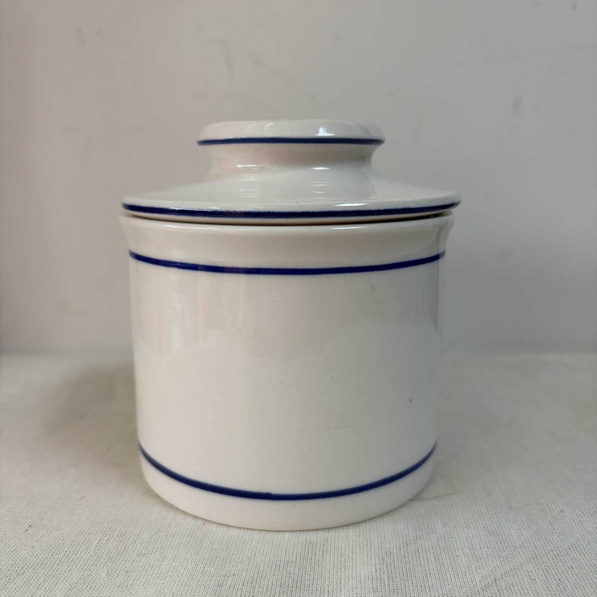 A white ceramic French butterbell or butter crock decorated with two thin blue horizontal stripes. 