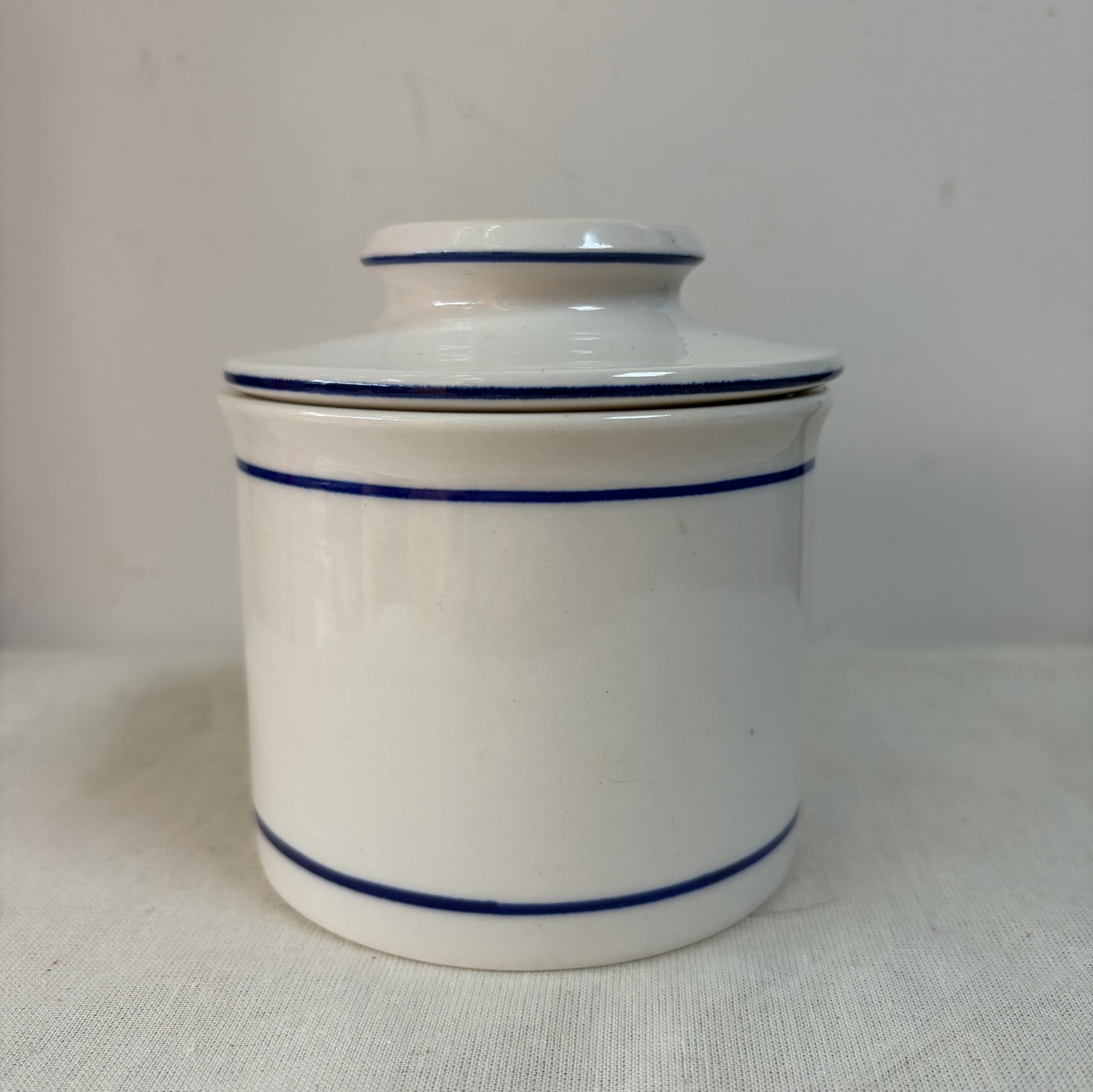 A white ceramic French butterbell or butter crock decorated with two thin blue horizontal stripes. 