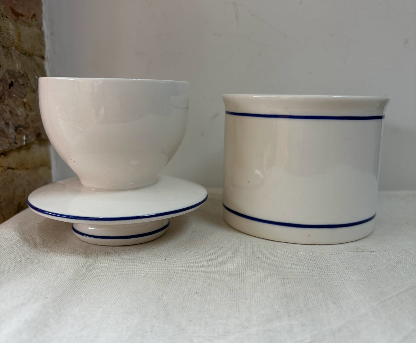 A white ceramic French butterbell or butter crock decorated with two thin blue horizontal stripes. 