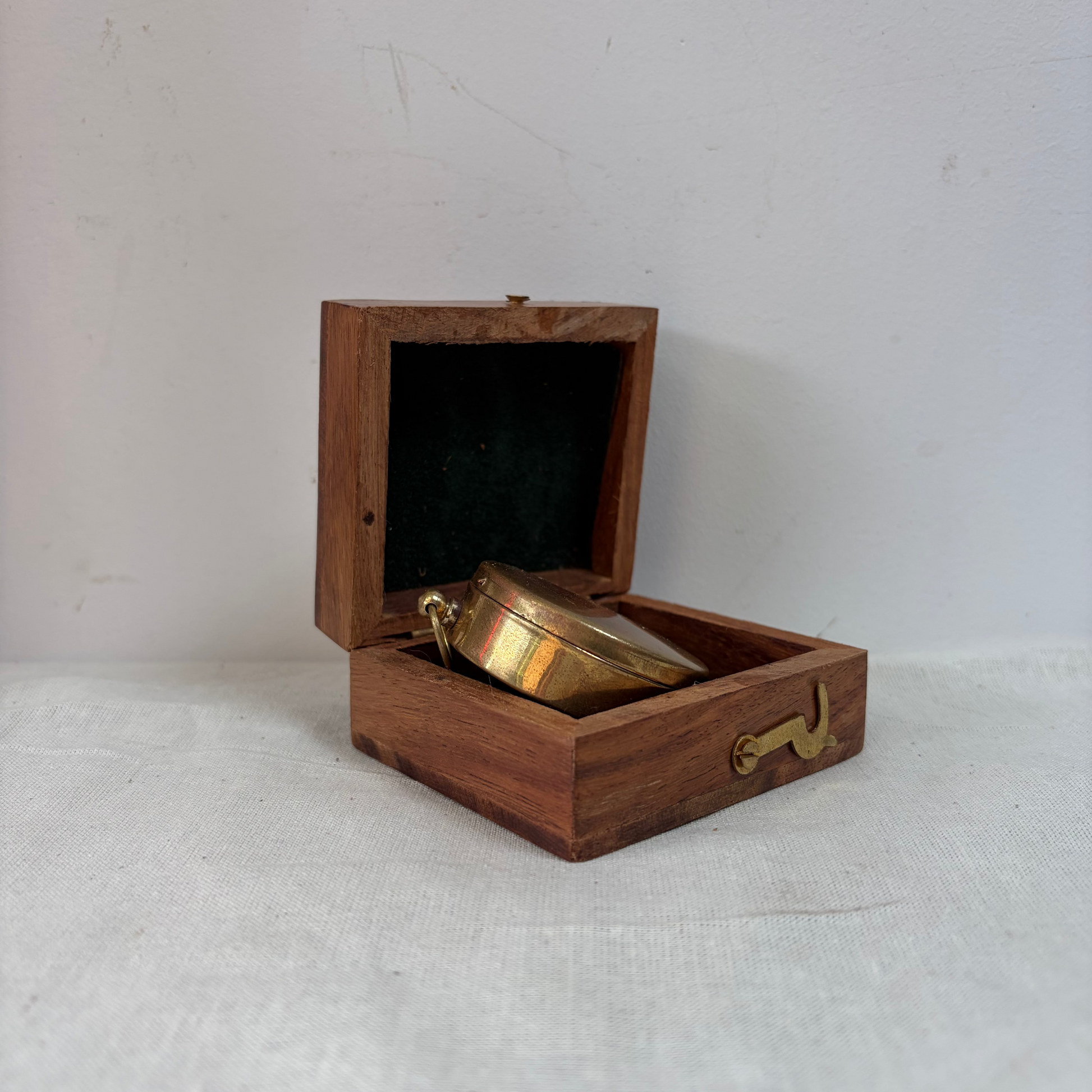 A small round brass pocket watch resting inside an open rectangular wooden presentation box.