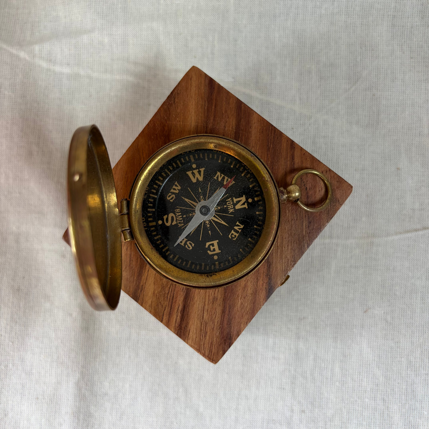 A small round brass pocket compass in an open rectangular wooden presentation box.