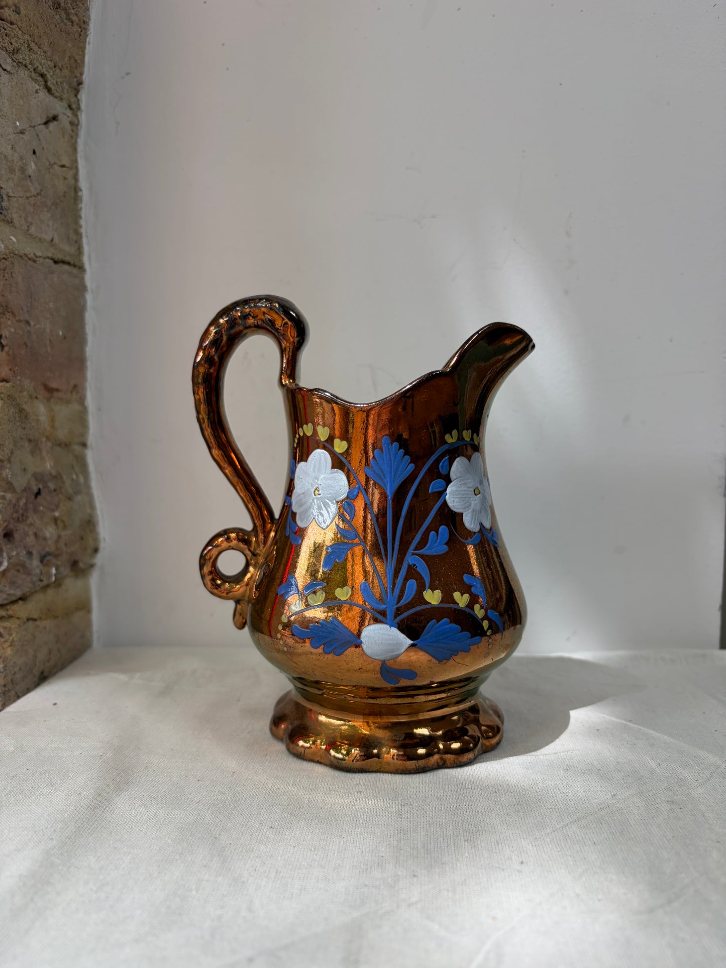 An ornate brown glass pitcher with a blue floral pattern and white flower accents. 