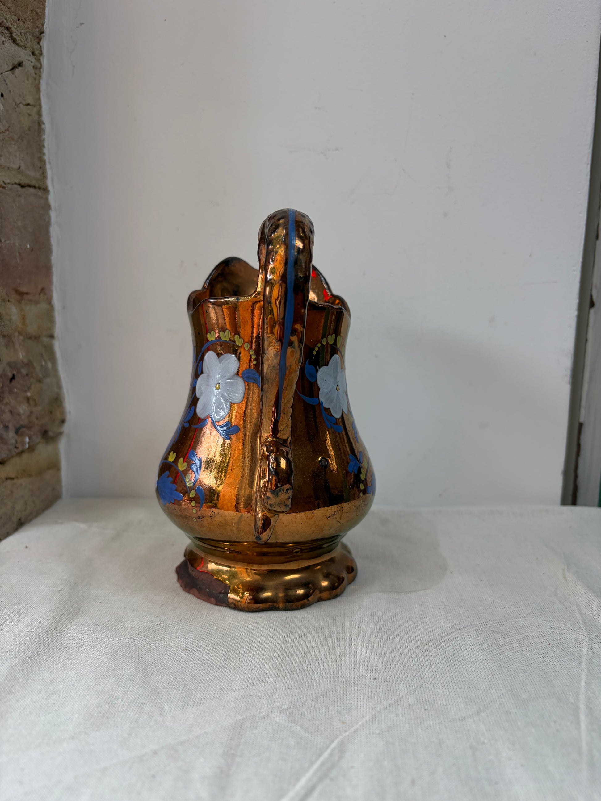 An antique iridescent gold pitcher with blue and white floral engravings. 