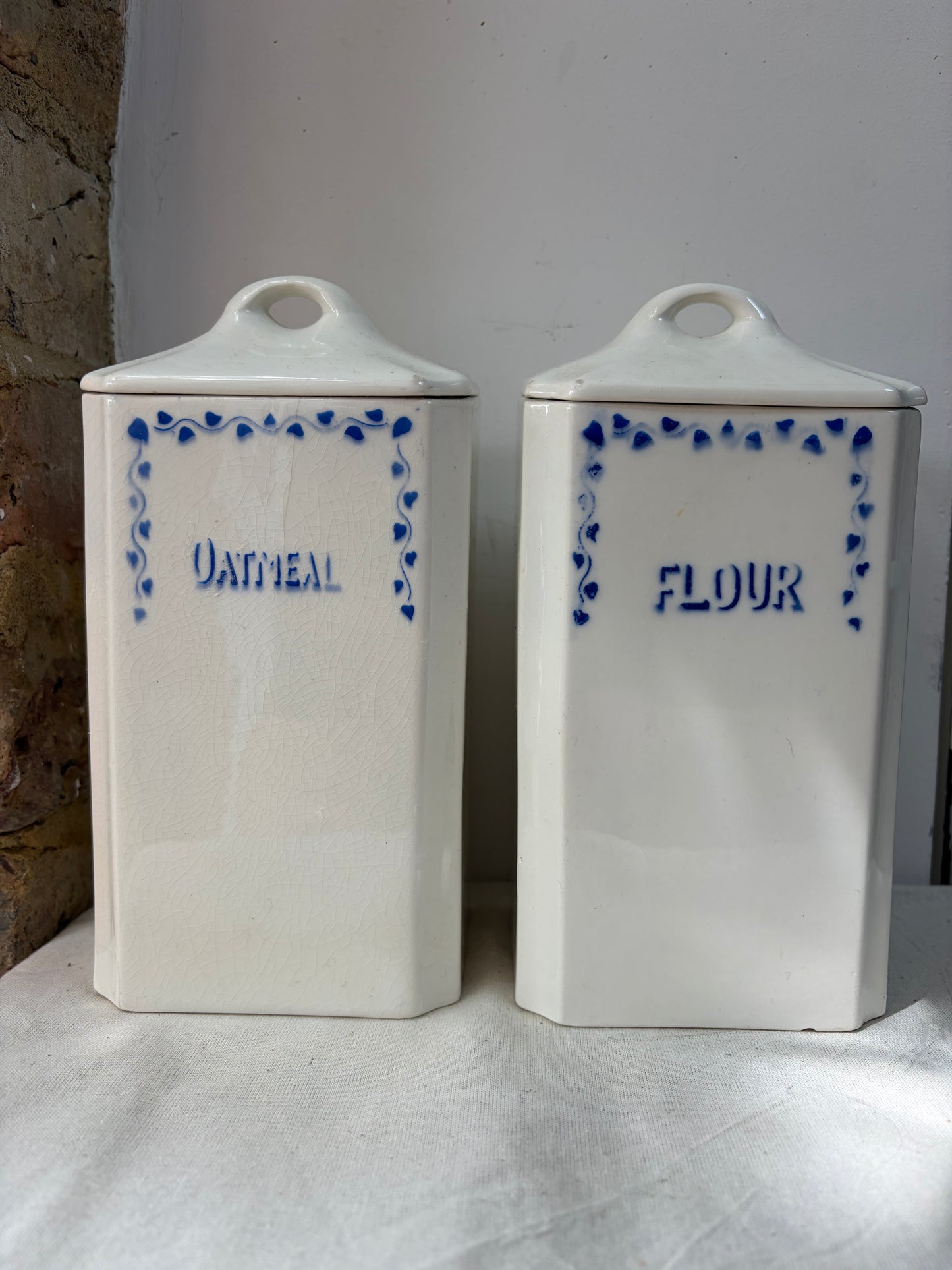 A pair of white kitchen storage jars  with blue decorative borders and labels reading 'OATMEAL' and 'FLOUR'. 