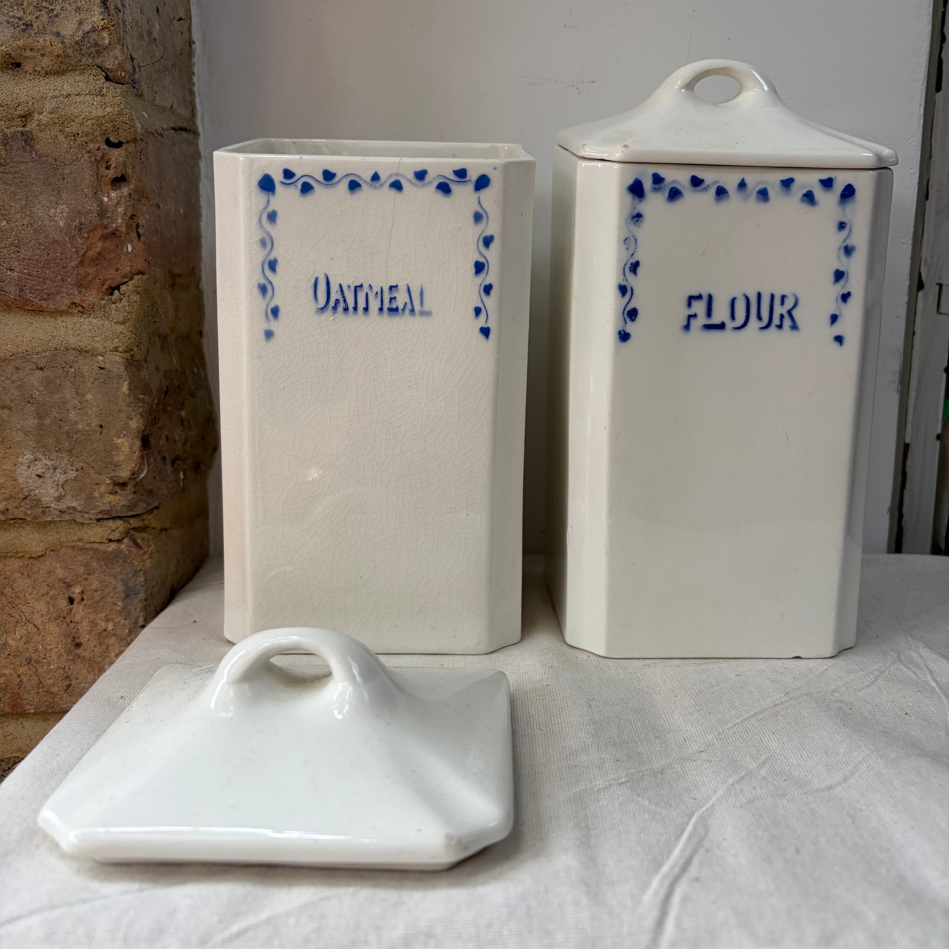 A pair of white kitchen storage jars  with blue decorative borders and labels reading 'OATMEAL' and 'FLOUR'. 