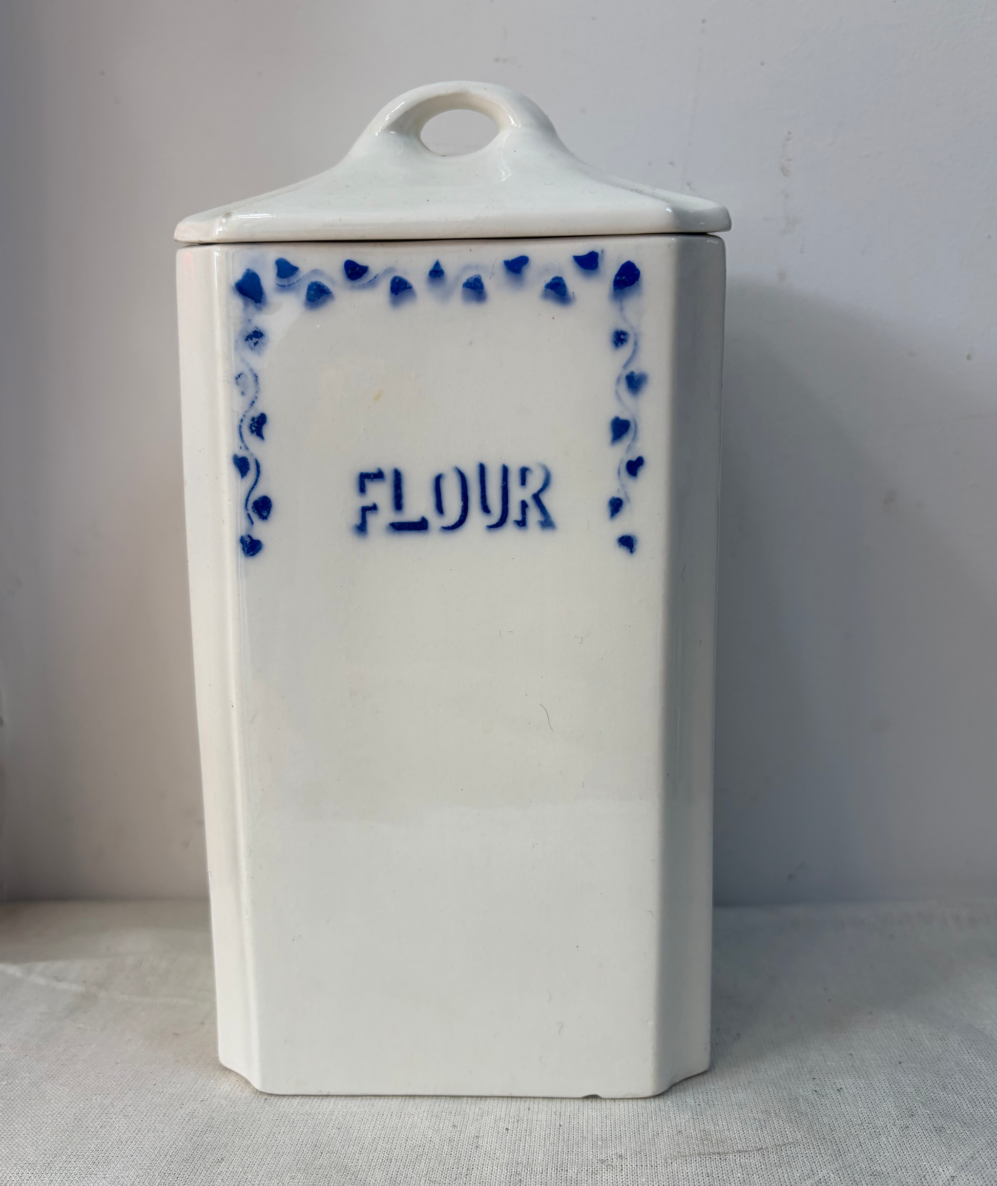 A pair of white kitchen storage jars  with blue decorative borders and labels reading 'OATMEAL' and 'FLOUR'. 