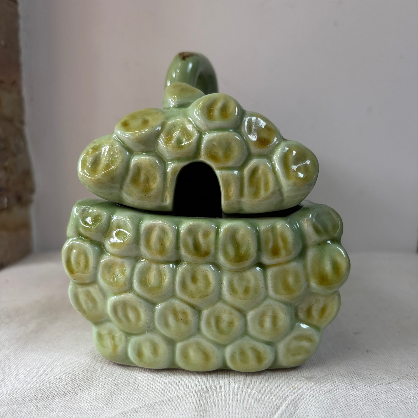 A ceramic asparagus dish, featuring a rectangular green glazed tray with a raised asparagus stem detail tied with a pink ribbon, displayed on a light fabric surface.